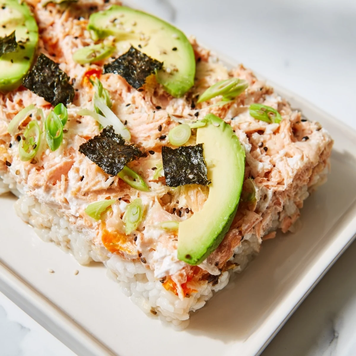 Warm sushi bake casserole bubbling in the oven, ready to be topped with fresh avocado slices.