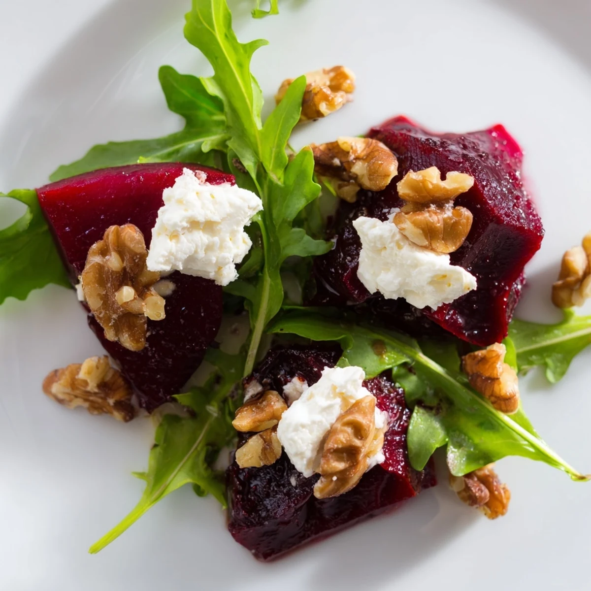 A close-up of roasted beet goat cheese salad with ruby beet wedges, crumbled cheese, and toasted walnuts on a bed of fresh arugula.