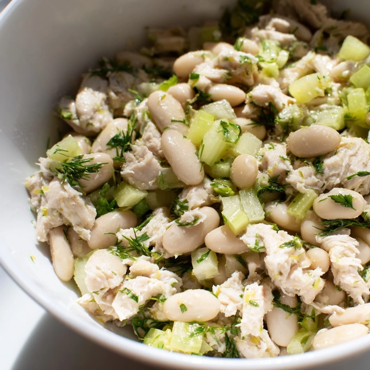 A close-up of the vibrant Lemony White Bean Chicken Salad, glistening with tangy lemon vinaigrette and fresh dill.  