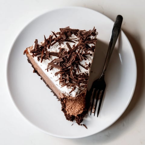 Sliced Lighter Chocolate Cottage Cheese Cheesecake reveals a creamy, cocoa-rich filling and dark chocolate shavings on top, served on a rustic plate.  