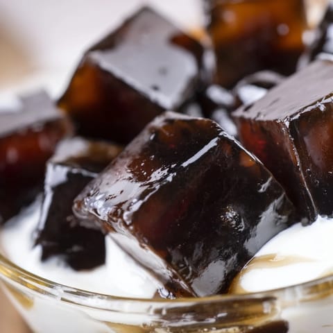 An overhead view of cut coffee jelly cubes gently resting in a bowl of vanilla cream.  