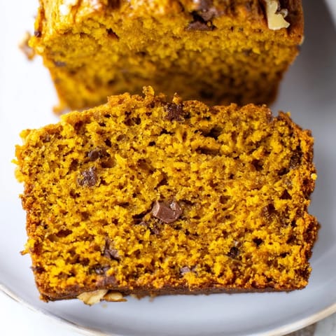 Slices of moist Pumpkin Bread Loaf with chocolate chips, served on a cozy wooden table.