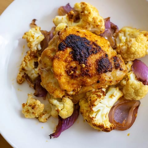 A single pan meal of seasoned chicken thighs and roasted cauliflower florets garnished with parsley and lemon.