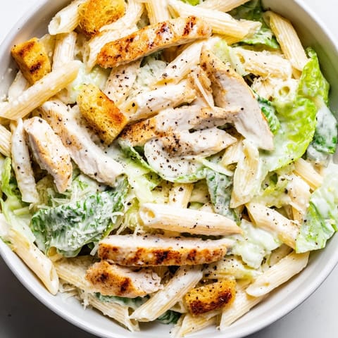 A close-up of a Caesar Pasta Chicken Bowl with al dente penne, juicy tomatoes, and crunchy garlic croutons.  