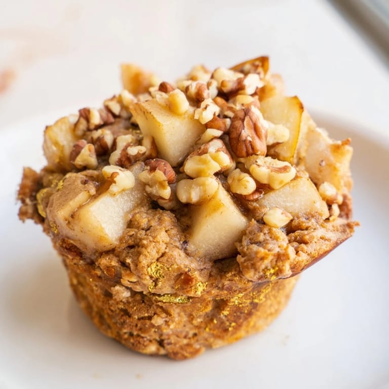 A close-up of warm, spiced pear and walnut muffins showcasing juicy pear pieces and walnuts within.