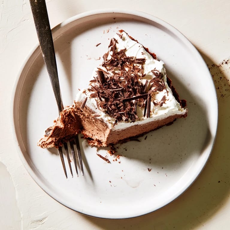 The Lighter Chocolate Cottage Cheese Cheesecake sits on a marble counter, showing a crumbly graham-cocoa crust and a dollop of Greek yogurt topping.