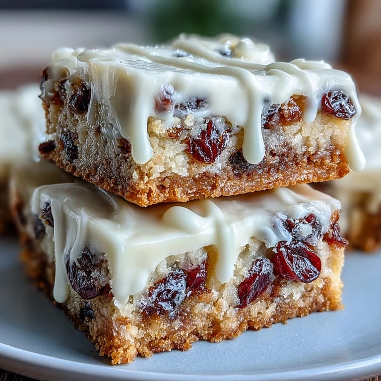 Holiday Cranberry Bliss Bars stacked on a plate with white chocolate drizzle, ready for dessert.