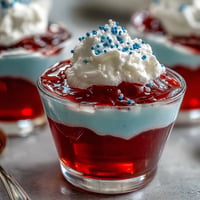 Vibrant 4th of July Firecracker Jello Shots shimmer, layered red, white, and blue.